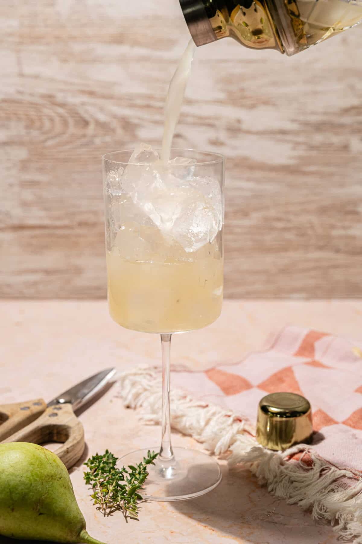 Pouring a pear cocktail from the shaker into a tall glass filled with crushed ice