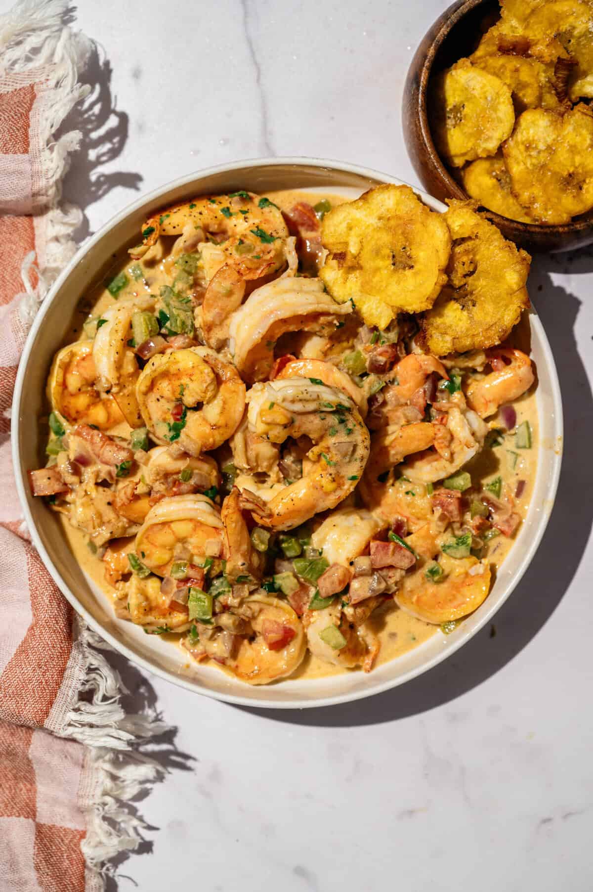 Overhead view of encocado de camarón in a white bowl with patacones on the side