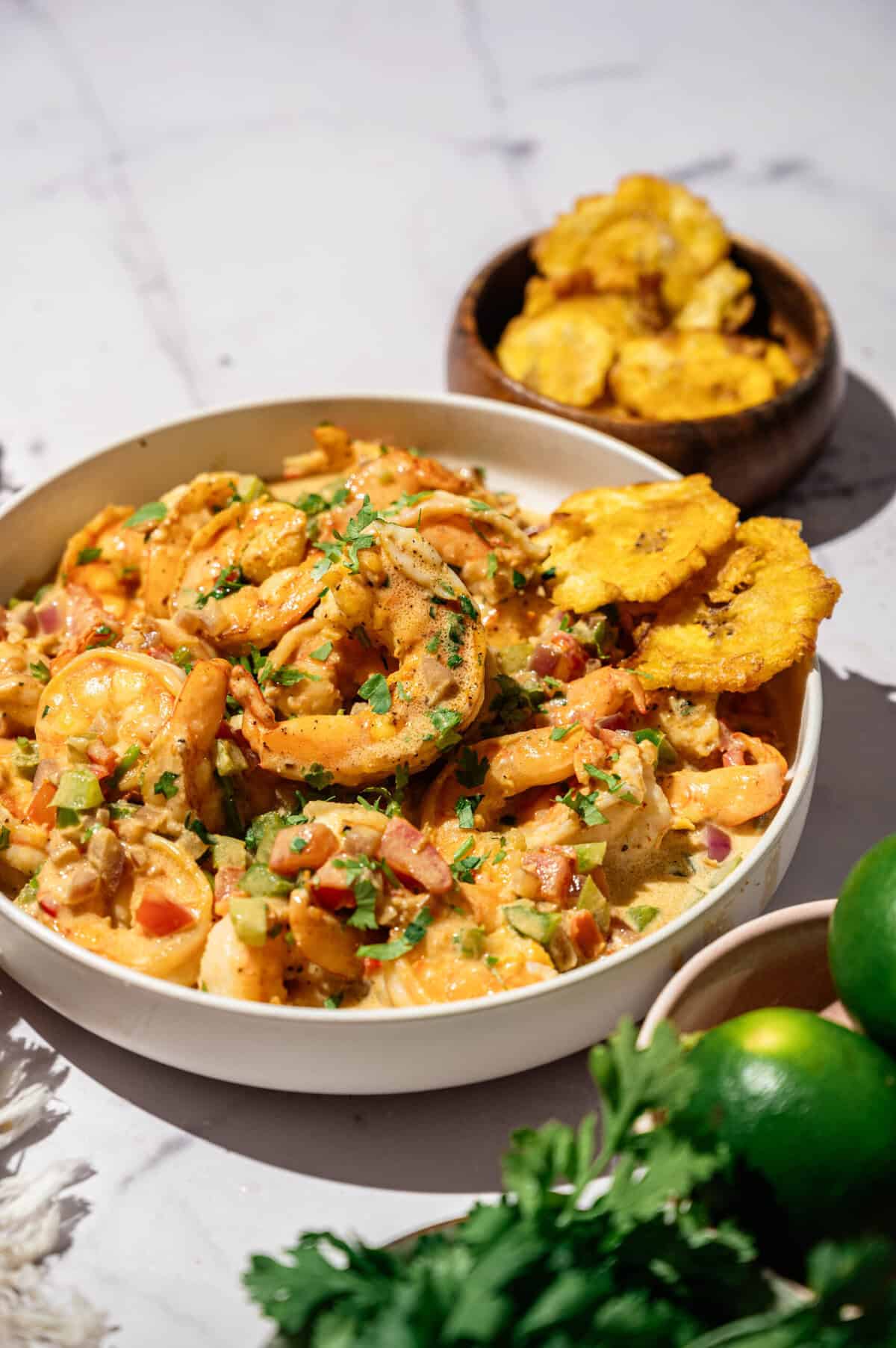 Encocado de camarón in a white bowl with patacones, limes, and fresh cilantro