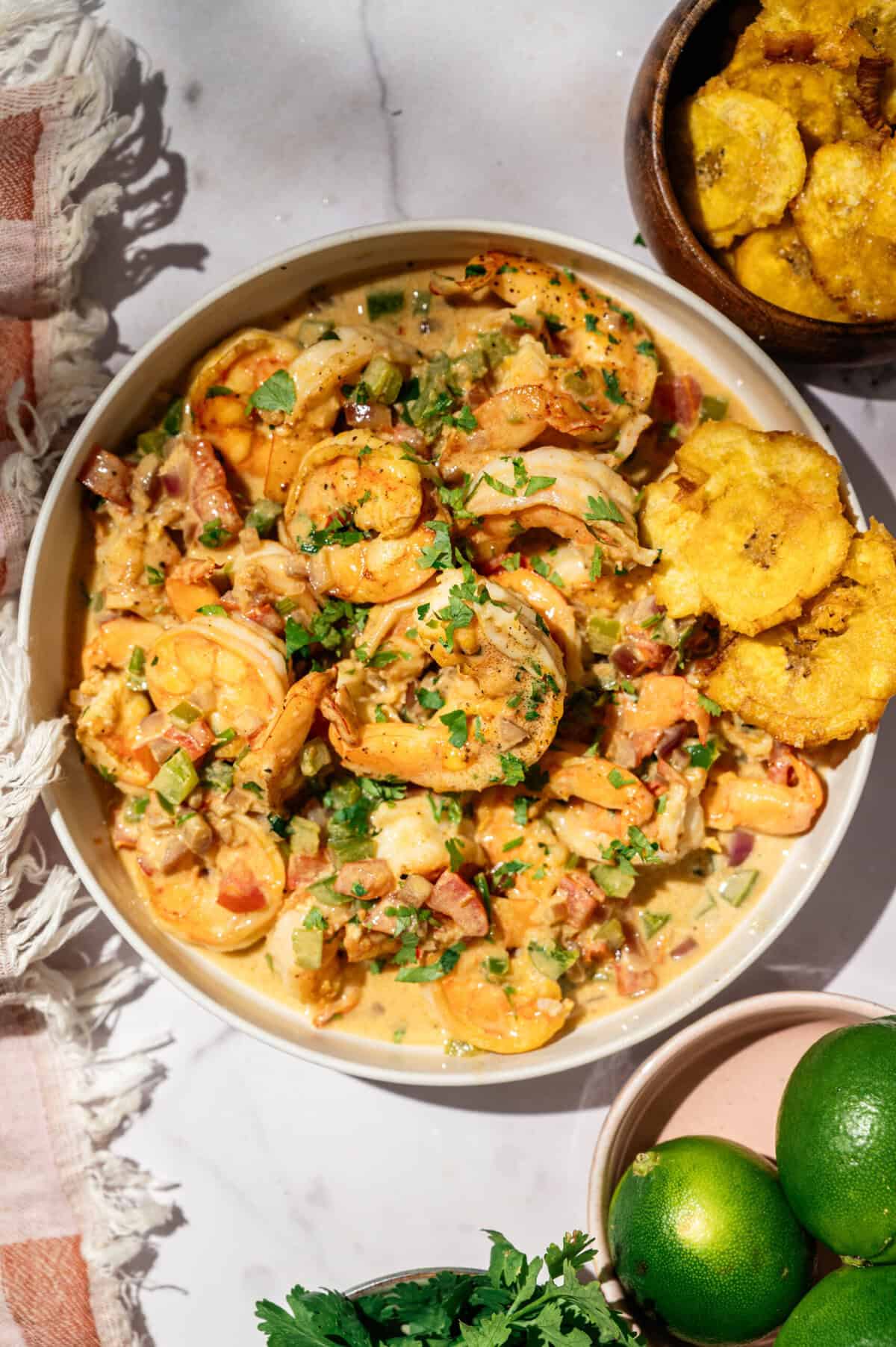 Overhead encocado de camarón with patacones, limes, and cilantro on a marble table