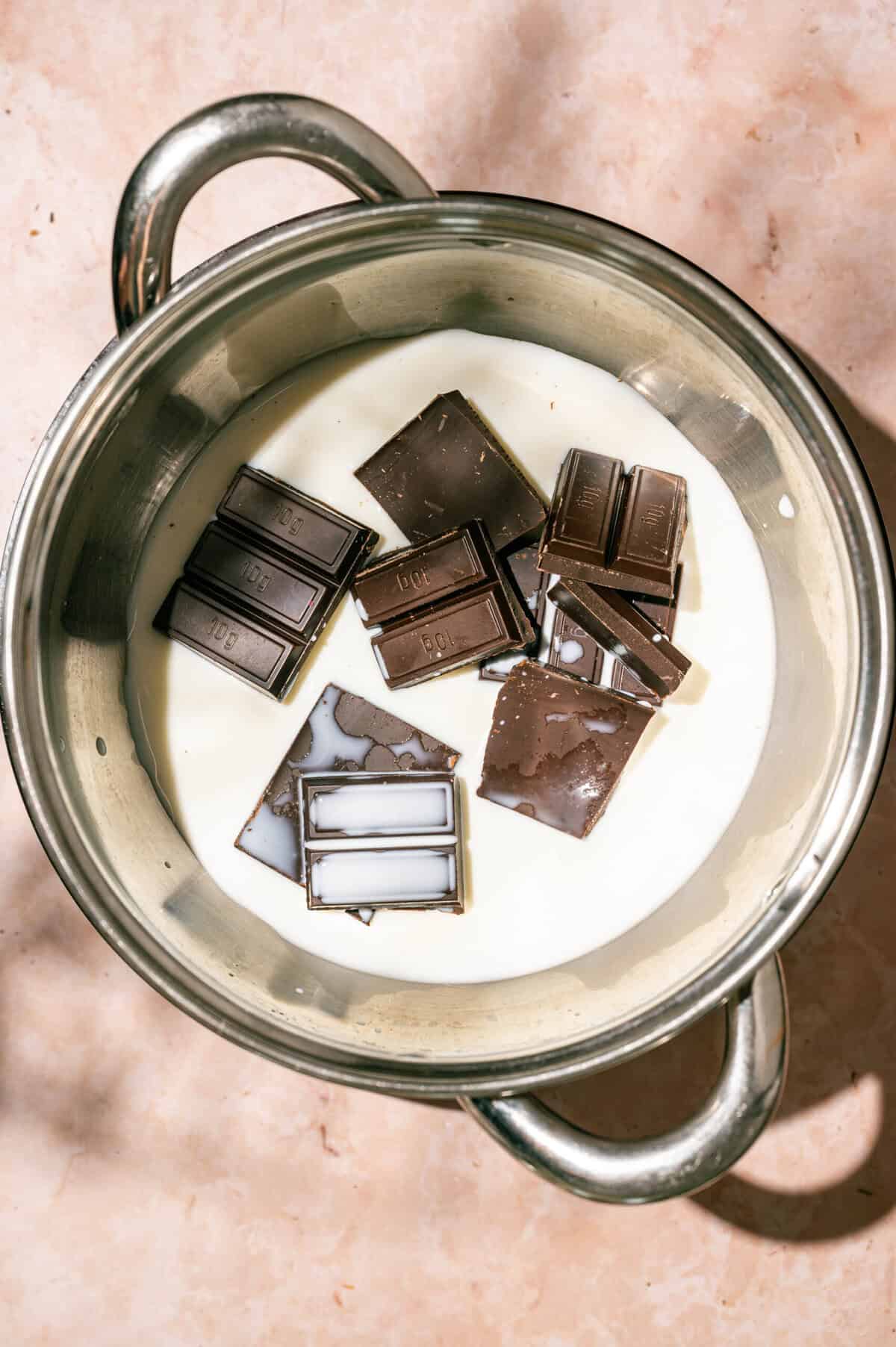 Pieces of dark chocolate bar in a saucepan of milk, the first step to making hot chocolate from scratch.
