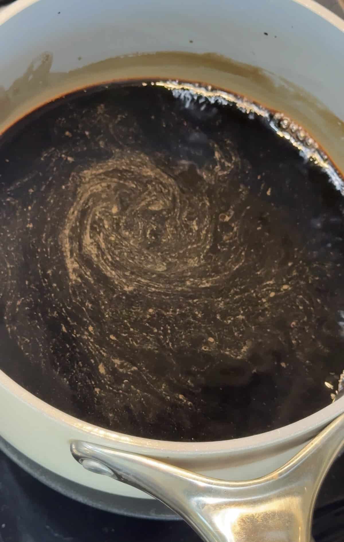 Balsamic vinegar simmering in a saucepan with light foam swirling on top as it reduces