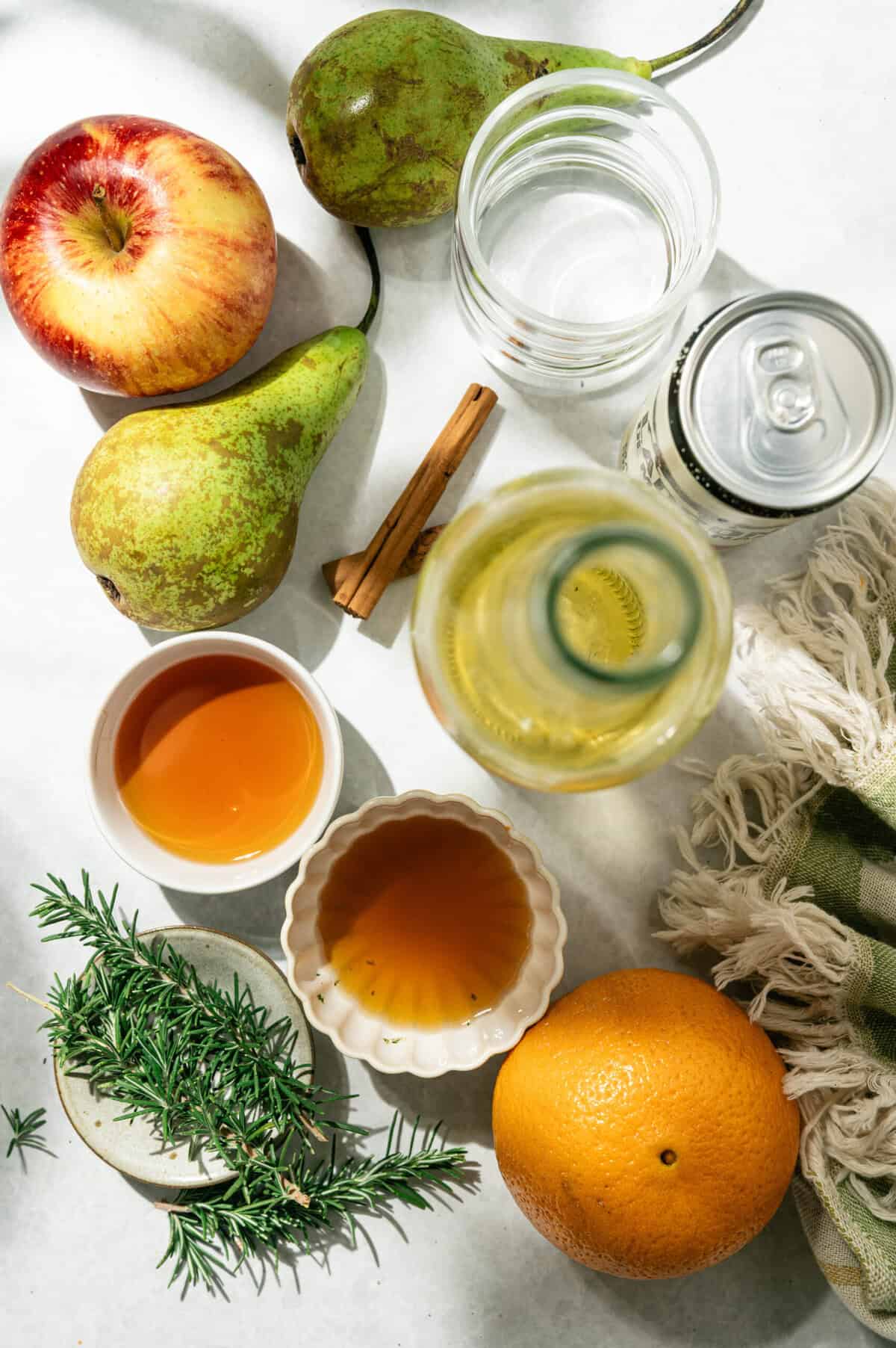Ingredients for apple cider sangria with pears: white wine, apple cider, brandy, honey, pears, apple, orange, cinnamon, and rosemary