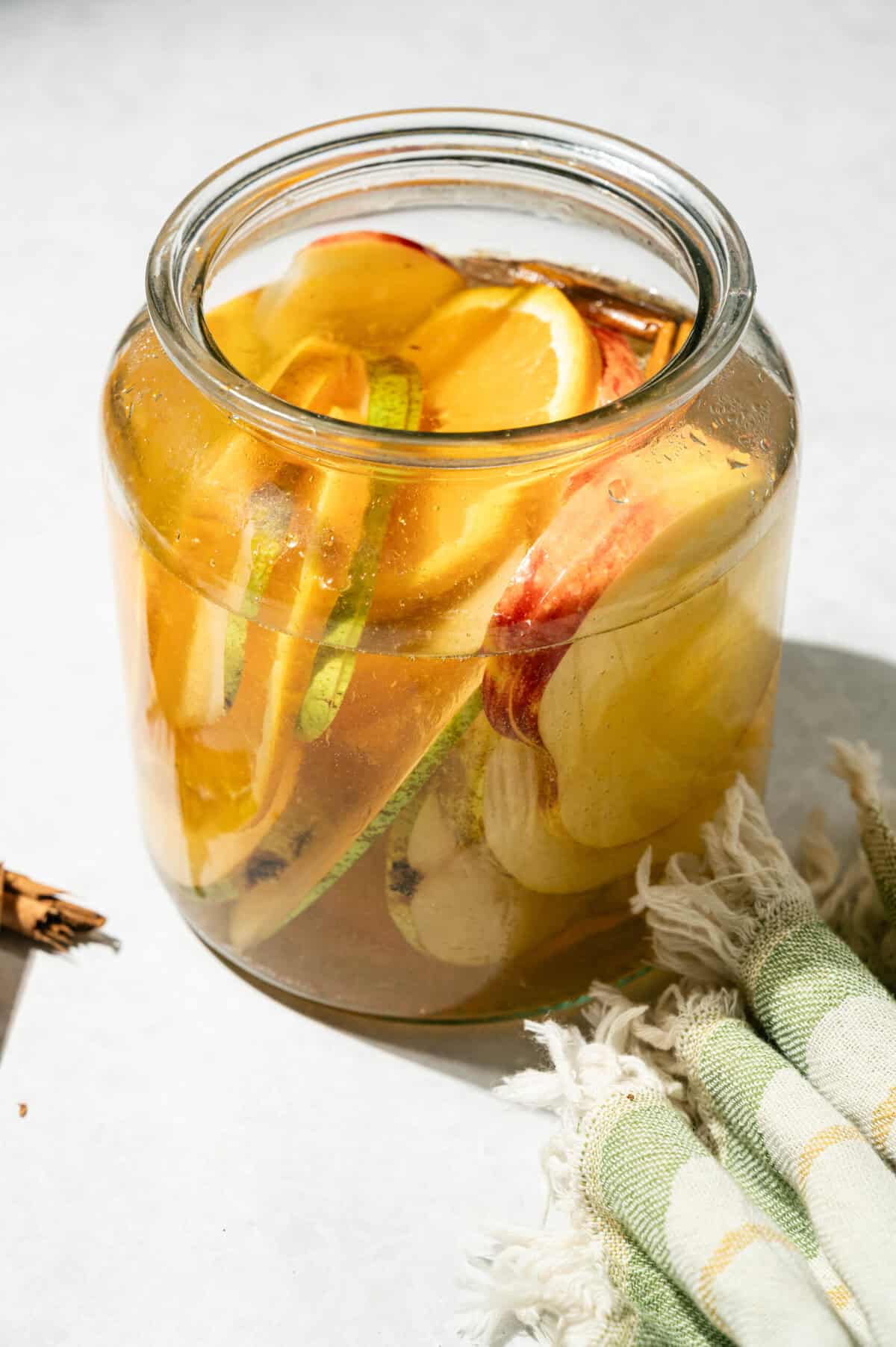 Apple cider sangria with pears, apple slices, oranges, and cinnamon sticks chilling in a large glass jar