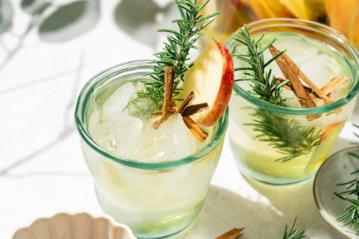 Two glasses of apple cider sangria with pears garnished with rosemary sprigs, cinnamon sticks, and apple slices