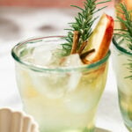 Glass of easy fall sangria over ice garnished with a rosemary sprig, cinnamon stick, and Honeycrisp apple slice