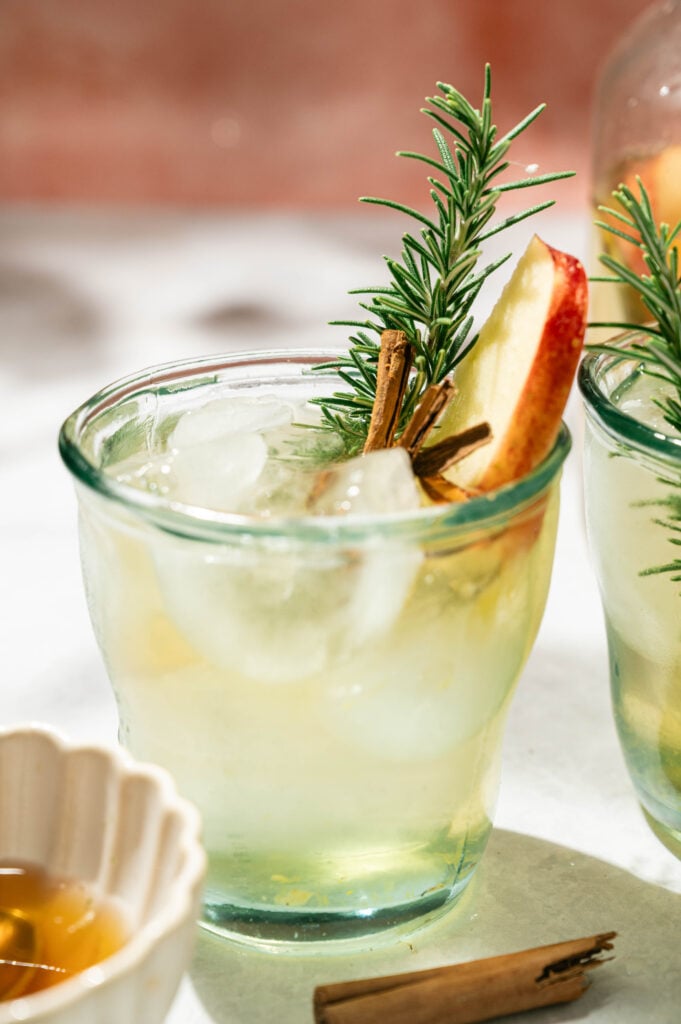 Glass of easy fall sangria over ice garnished with a rosemary sprig, cinnamon stick, and Honeycrisp apple slice