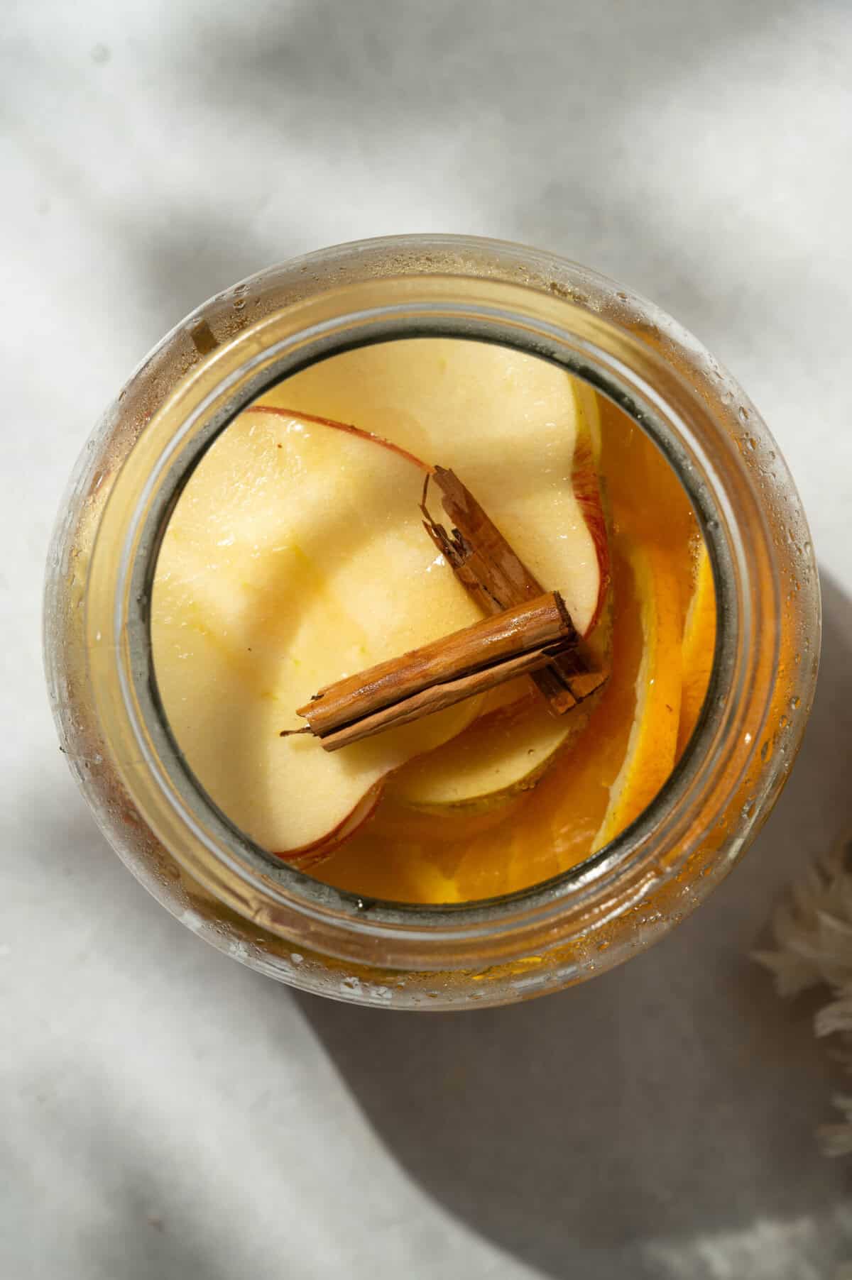 Overhead view of apple cider sangria with pears, Honeycrisp apple slices, orange, and cinnamon sticks in a glass jar