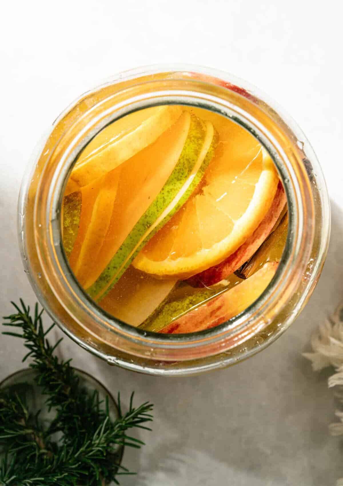 Sliced pears, Honeycrisp apples, and orange layered in a large glass jar to start apple cider sangria
